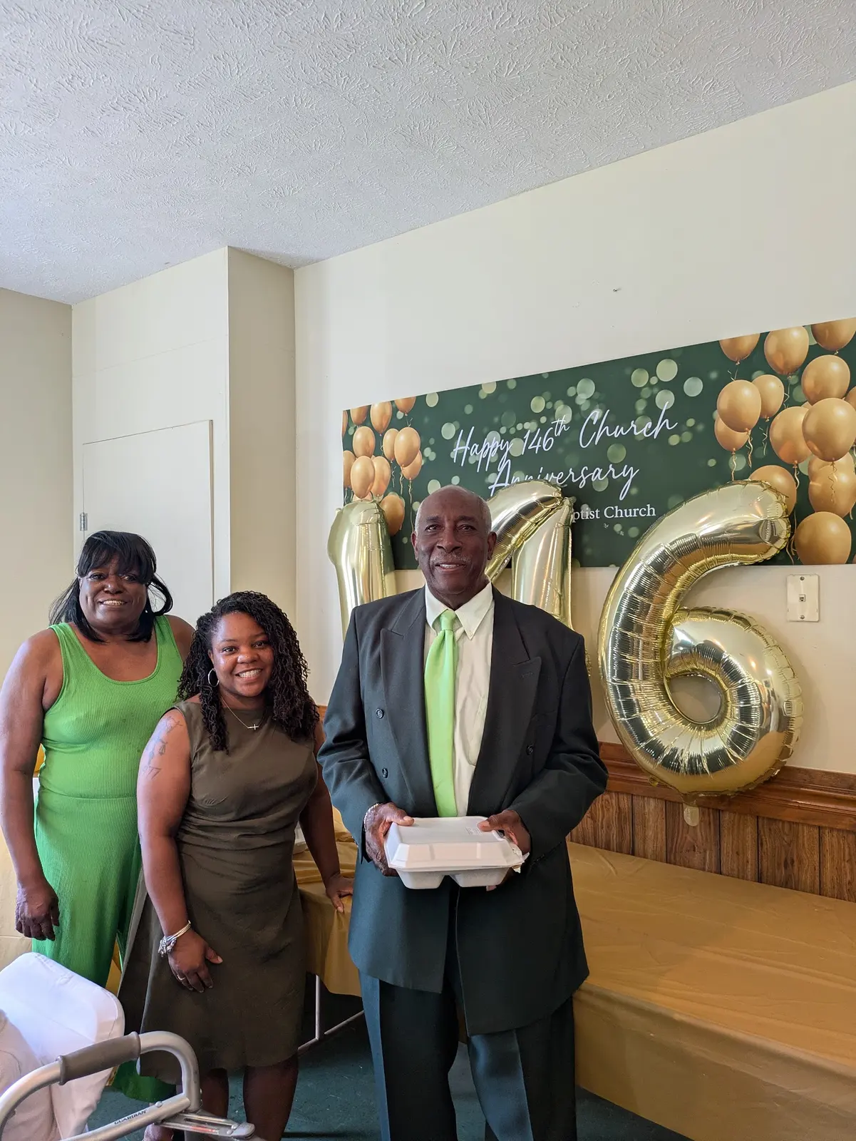 Three members smiling beside the gold 146 balloons at the church's 146th anniversary