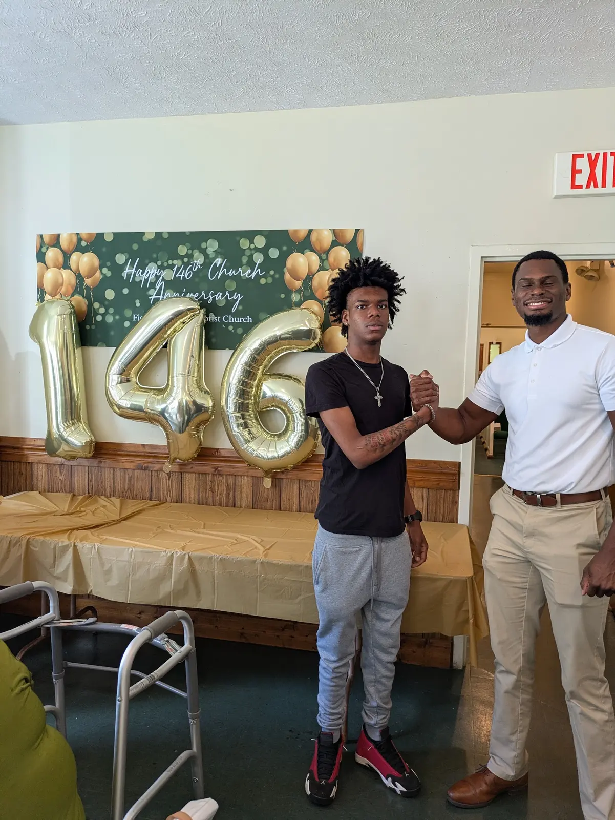 Two young men shaking hands in front of the 146th anniversary balloons