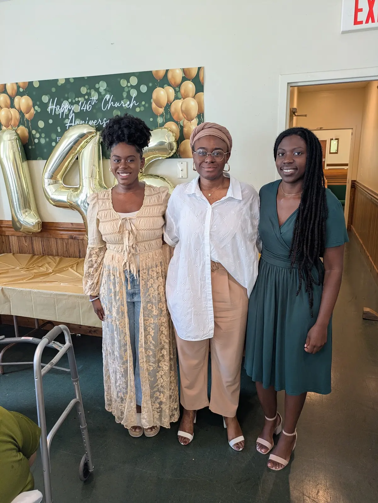 Three women smiling in front of the anniversary backdrop
