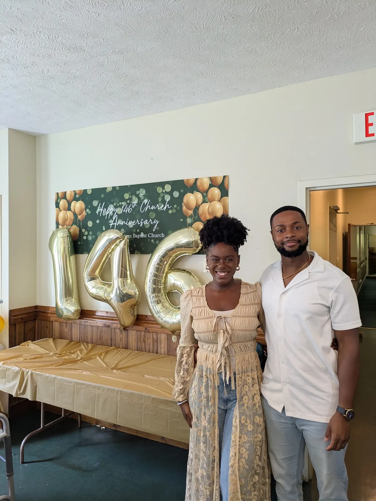 A couple posing in front of the gold 146 balloons