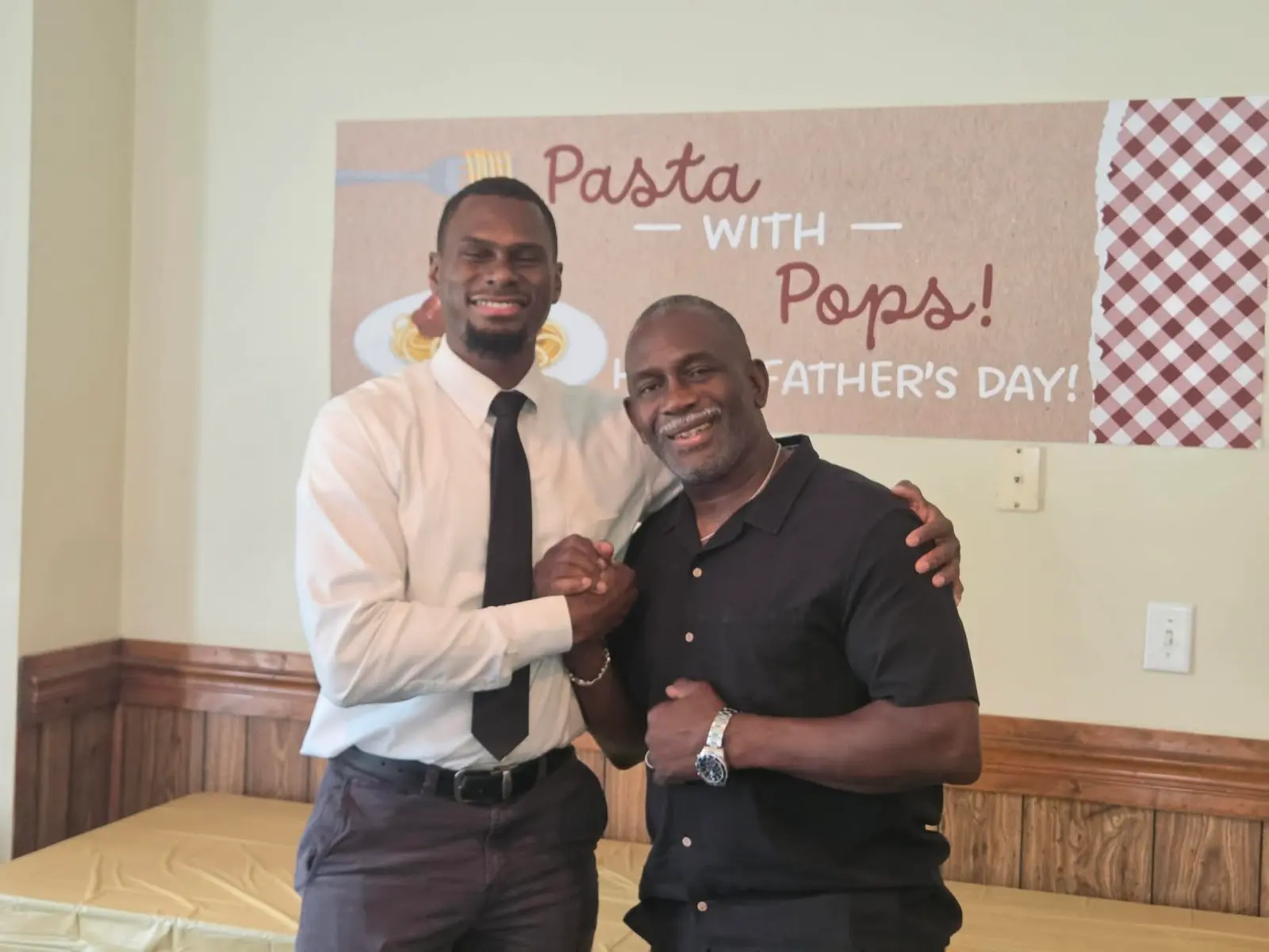 Two men embracing in front of the Father's Day banner