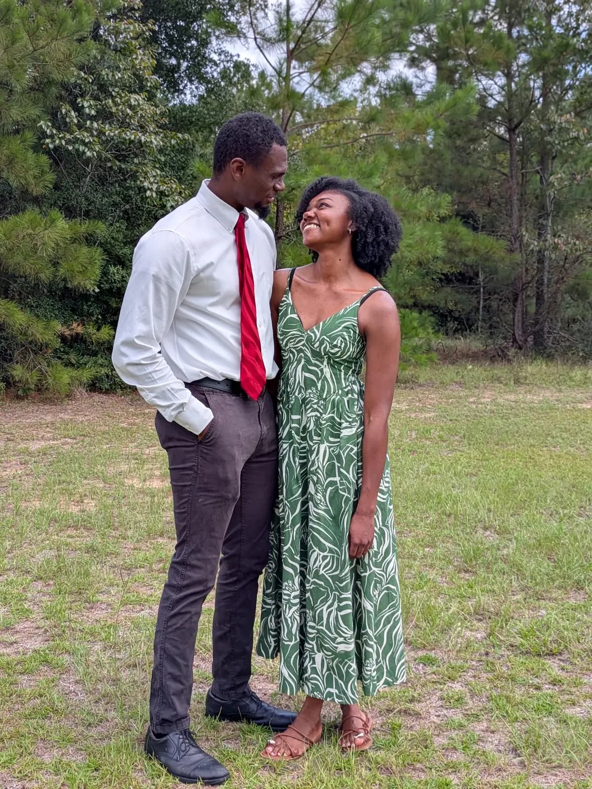 A young couple smiling outdoors in front of the pines