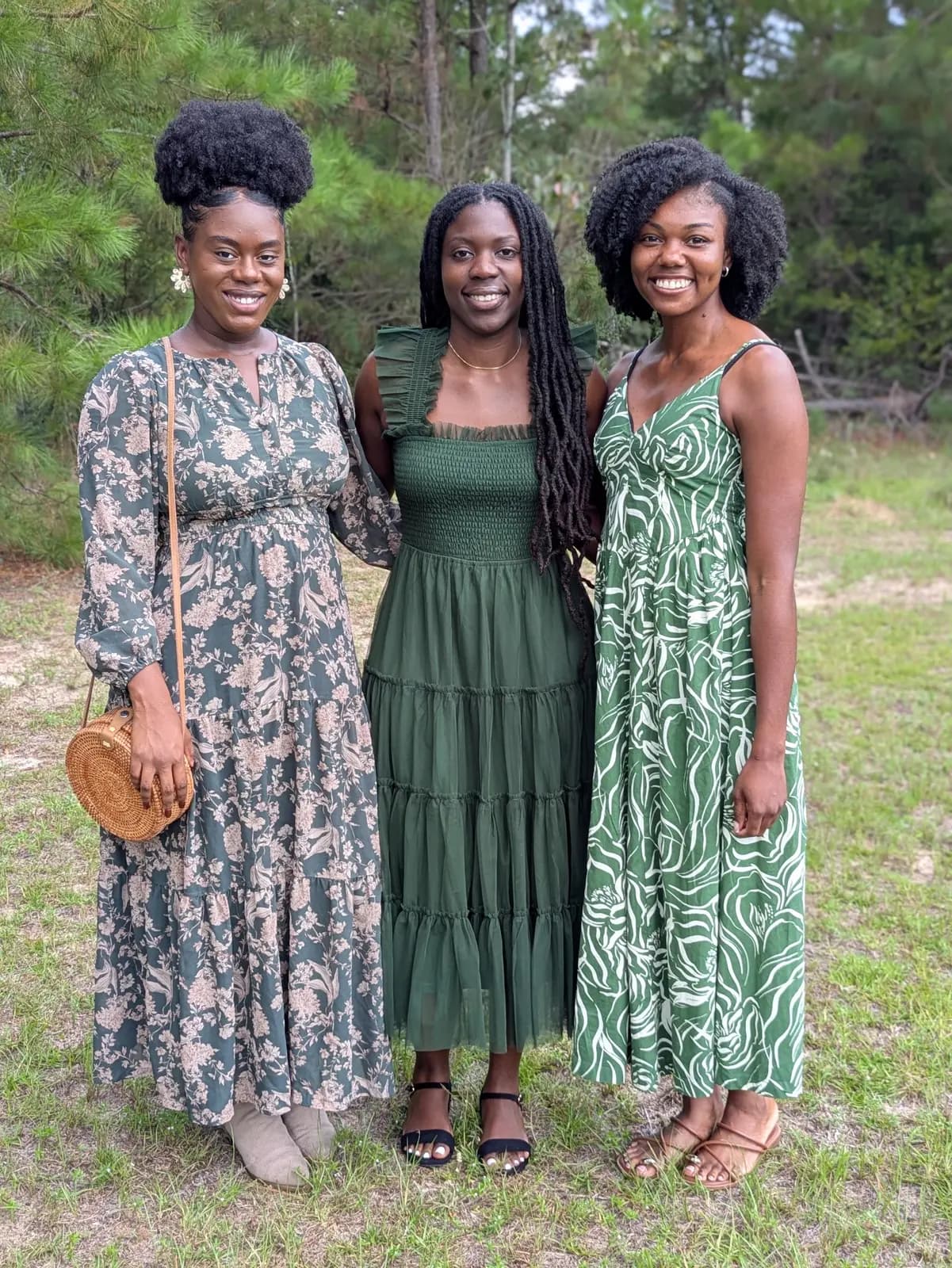 Three women in sundresses posing in a grassy field