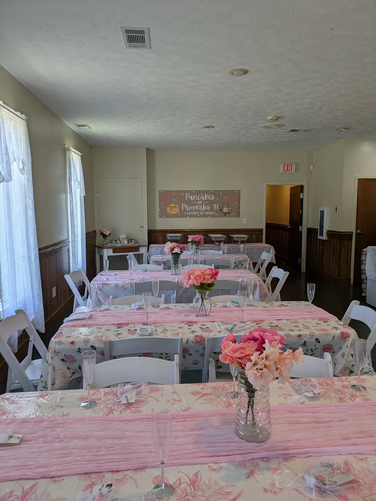 Fellowship hall tables set with floral cloths and pink roses for the Mother's Day brunch
