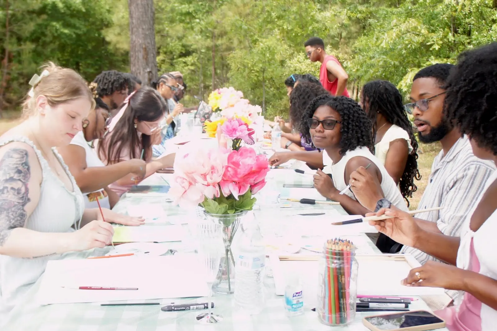 Members painting together at a long picnic table outdoors