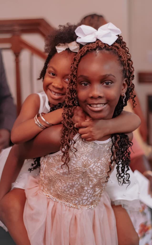 Two girls smiling together at church in coordinated dresses and hair bows.