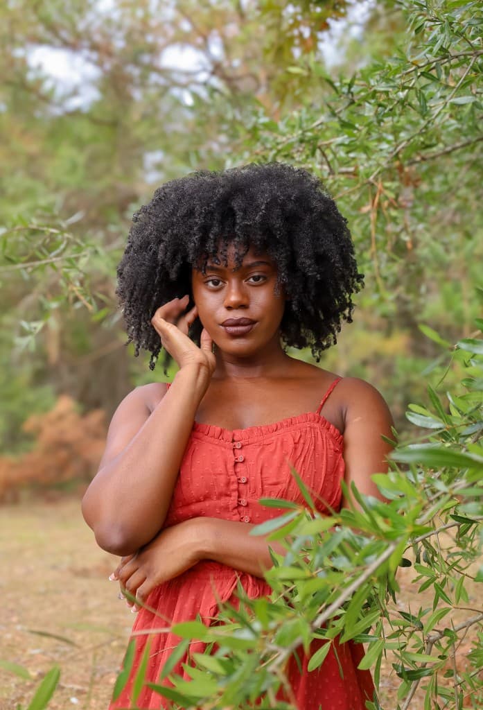 Church member in a red dress posing outside near trees and greenery.