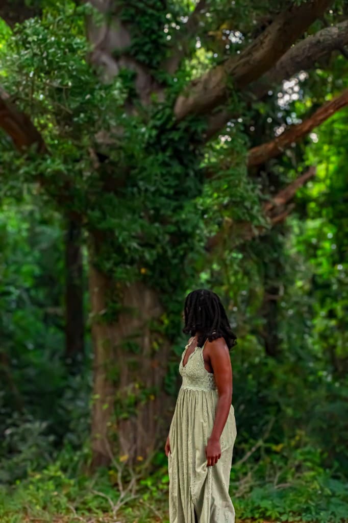 Church member in a light green dress standing in a wooded area.